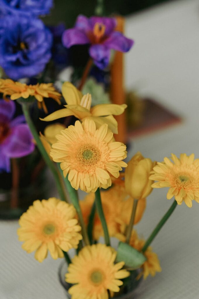 Vibrant yellow gerbera daisies arranged with other flowers on a table, creating a bright and decorative floral display.
